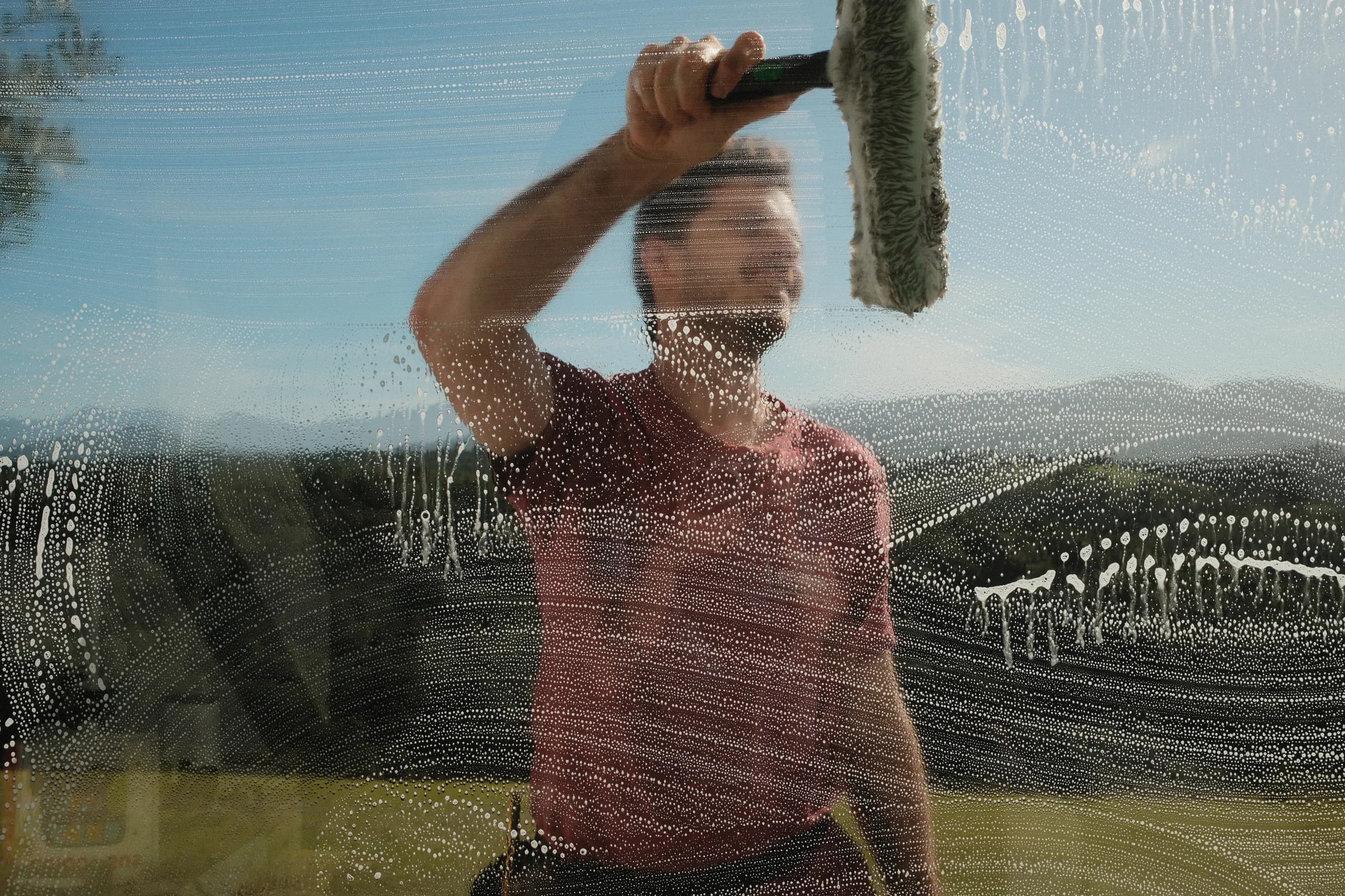 Close-up through soapy glass of a ProWash team member washing a window, Knysna hills behind